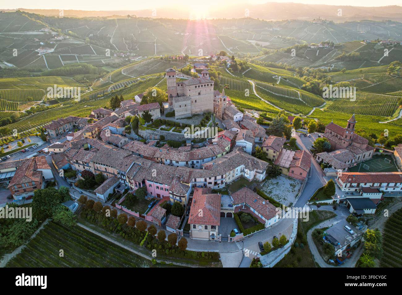Vista aerea dello storico castello di Serralunga d'Alba circondato da lussureggianti vigneti e dolci colline della regione Piemonte al tramonto a Serralunga Foto Stock