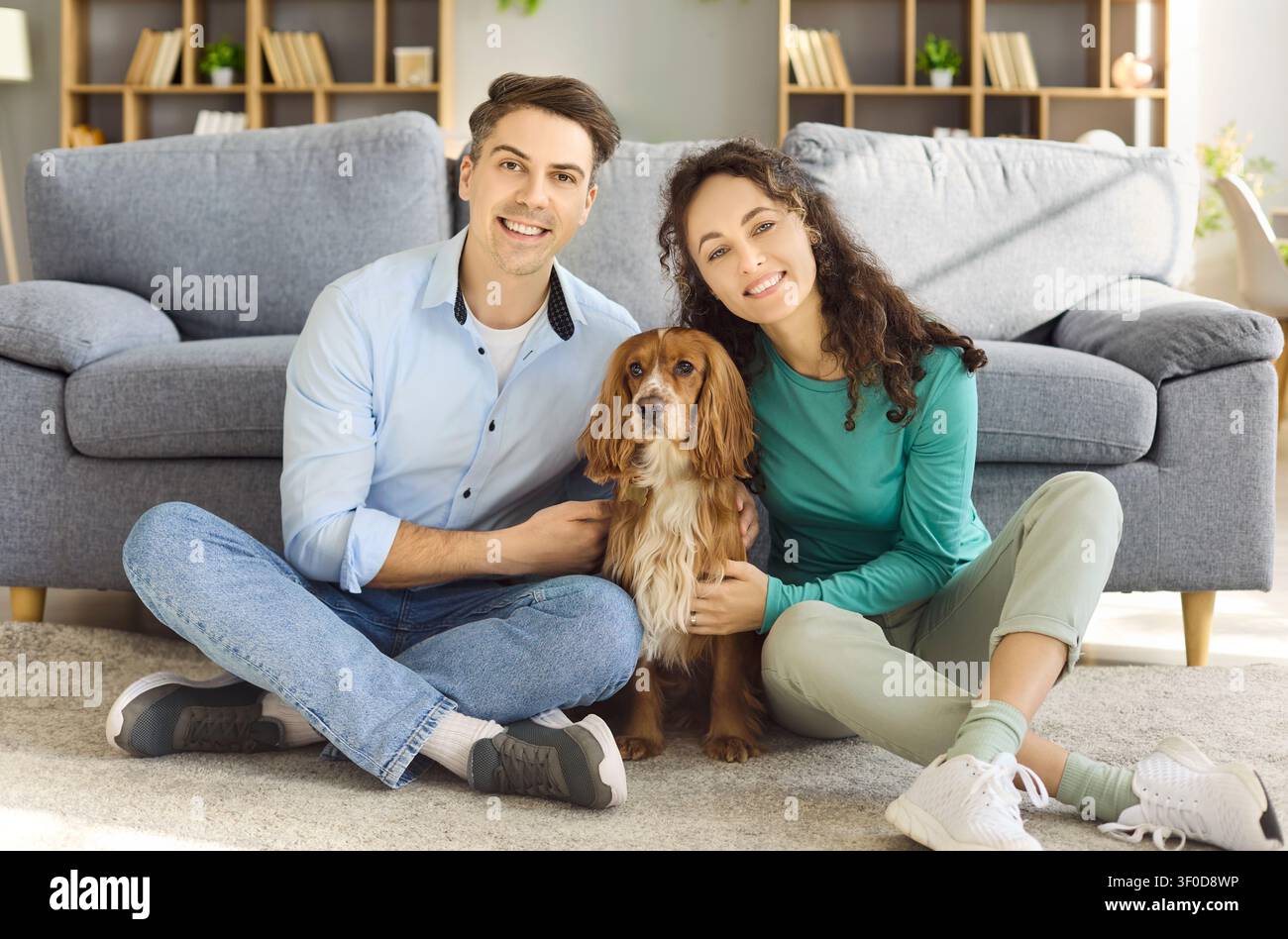 Giovane coppia felice con un cocker spaniel che si rilassa sul pavimento del soggiorno a casa Foto Stock
