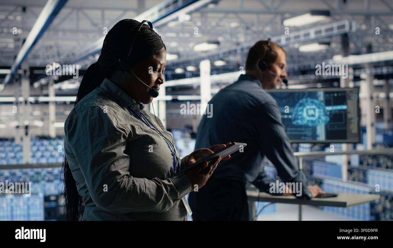 L'amministratore di sistema afroamericano utilizza l'intelligenza artificiale su un tablet in una server farm per aiutare i clienti a risolvere i problemi di hosting del sito Web. Foto Stock
