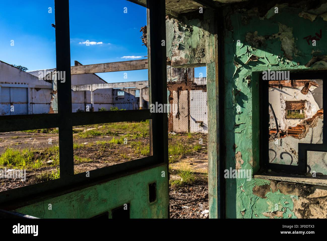 Vista interna di un edificio abbandonato e in rovina con vernice verde scrostata sulle pareti. Una vista attraverso le cornici delle finestre in cemento mostra un luogo completamente abbandon Foto Stock
