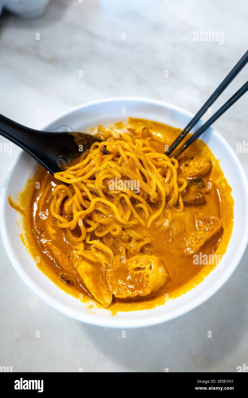 Spaghetti Ipoh Curry Mee sollevati con le bacchette da un ricco brodo di curry al cocco. Foto Stock