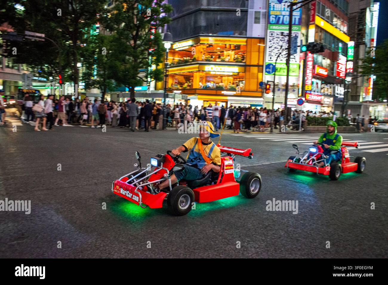 Turisti che guidano go-kart a tema attraverso il famoso Shibuya Crossing a Shibuya, circondati da luci al neon e folle di notte, Tokyo, Giappone. Shibuya Foto Stock