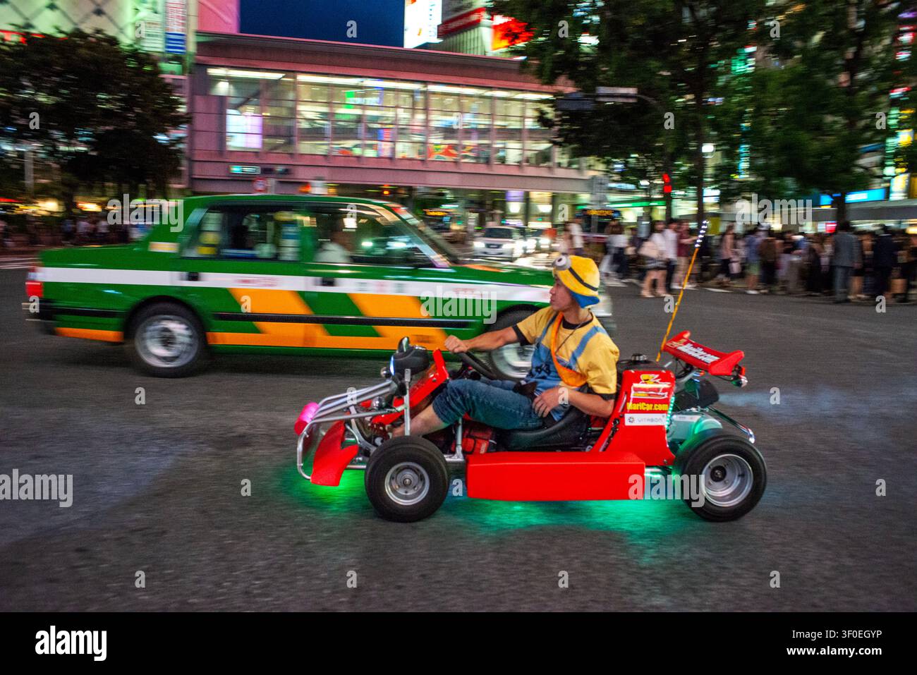 Turisti che guidano go-kart a tema attraverso il famoso Shibuya Crossing a Shibuya, circondati da luci al neon e folle di notte, Tokyo, Giappone. Shibuya Foto Stock