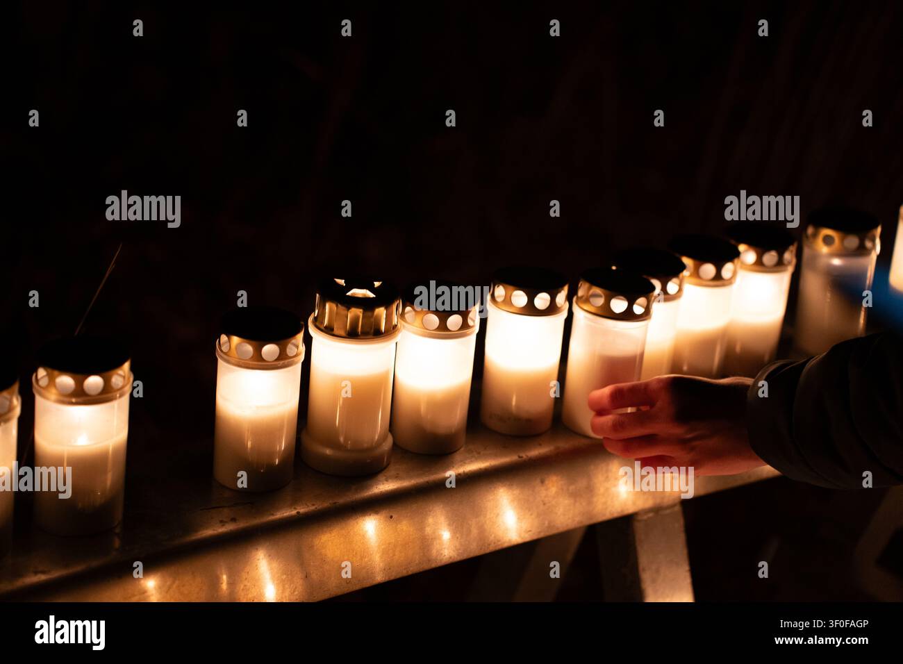 Persona che tiene una candela commemorativa accesa all'aperto di notte con candele luminose sullo sfondo, Ognissanti al cimitero di Skogskyrkogarden a Stoccolma, Svezia Foto Stock