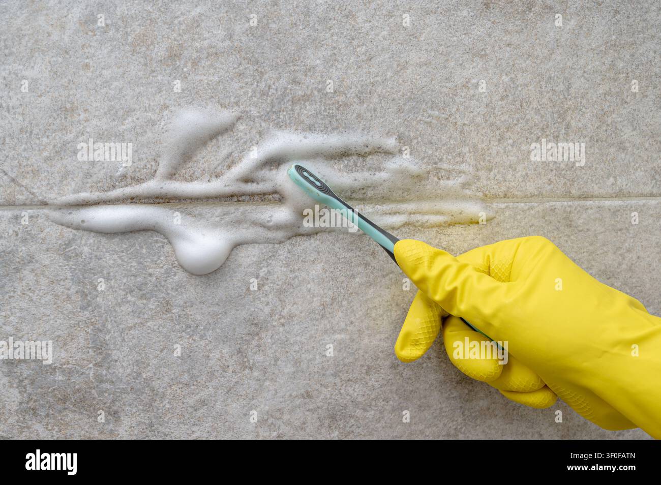 Pulizia delle fughe delle piastrelle del bagno con spazzolino da denti e schiuma bianca Foto Stock