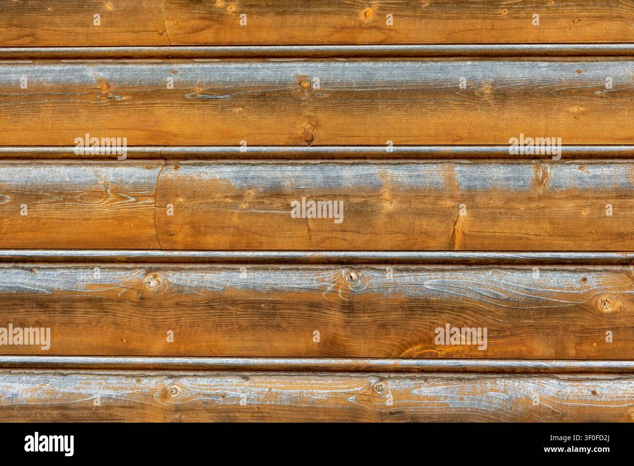 Texture di rivestimento in assi di legno stagionate. Assi di legno orizzontali mostrano venature marrone calde, nodi, striature grigie stagionate, cuciture e una texture rustica del rivestimento Foto Stock