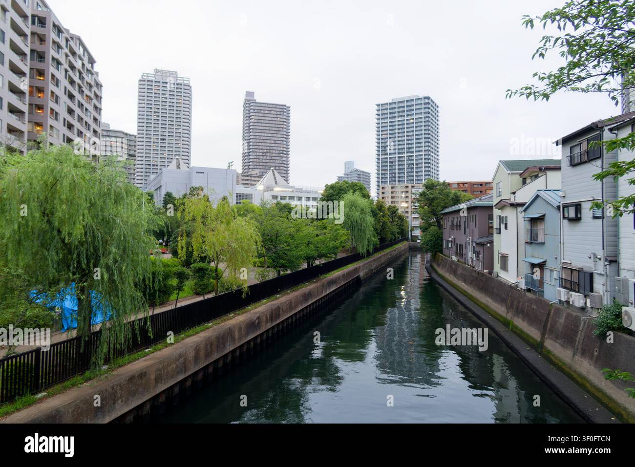 Canale storico a Tsukuda, Tokyo, dove le case tradizionali di Shitamachi, i corsi d'acqua tranquilli e le moderne torri residenziali creano un paesaggio urbano unico che collega Foto Stock