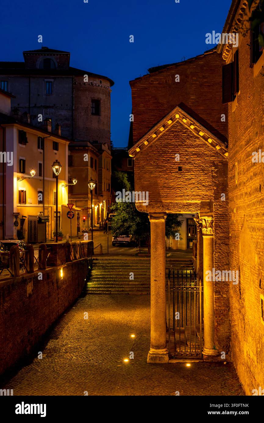 Vista notturna del portico d’ingresso del chiostro di San Clemente con la torre medievale del monastero Santi Quattro Coronati sullo sfondo. Roma, Italia. Foto Stock