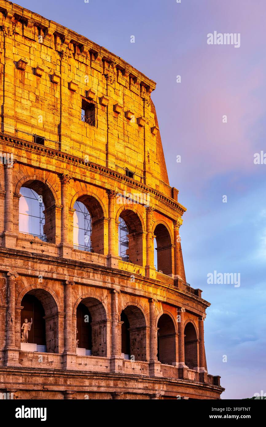 Prima piano del Colosseo (Amphitheatrum Flavium) illuminato dalla calda luce del tramonto, che mostra tre ordini di archi su un cielo rosa. Roma, Italia. Foto Stock