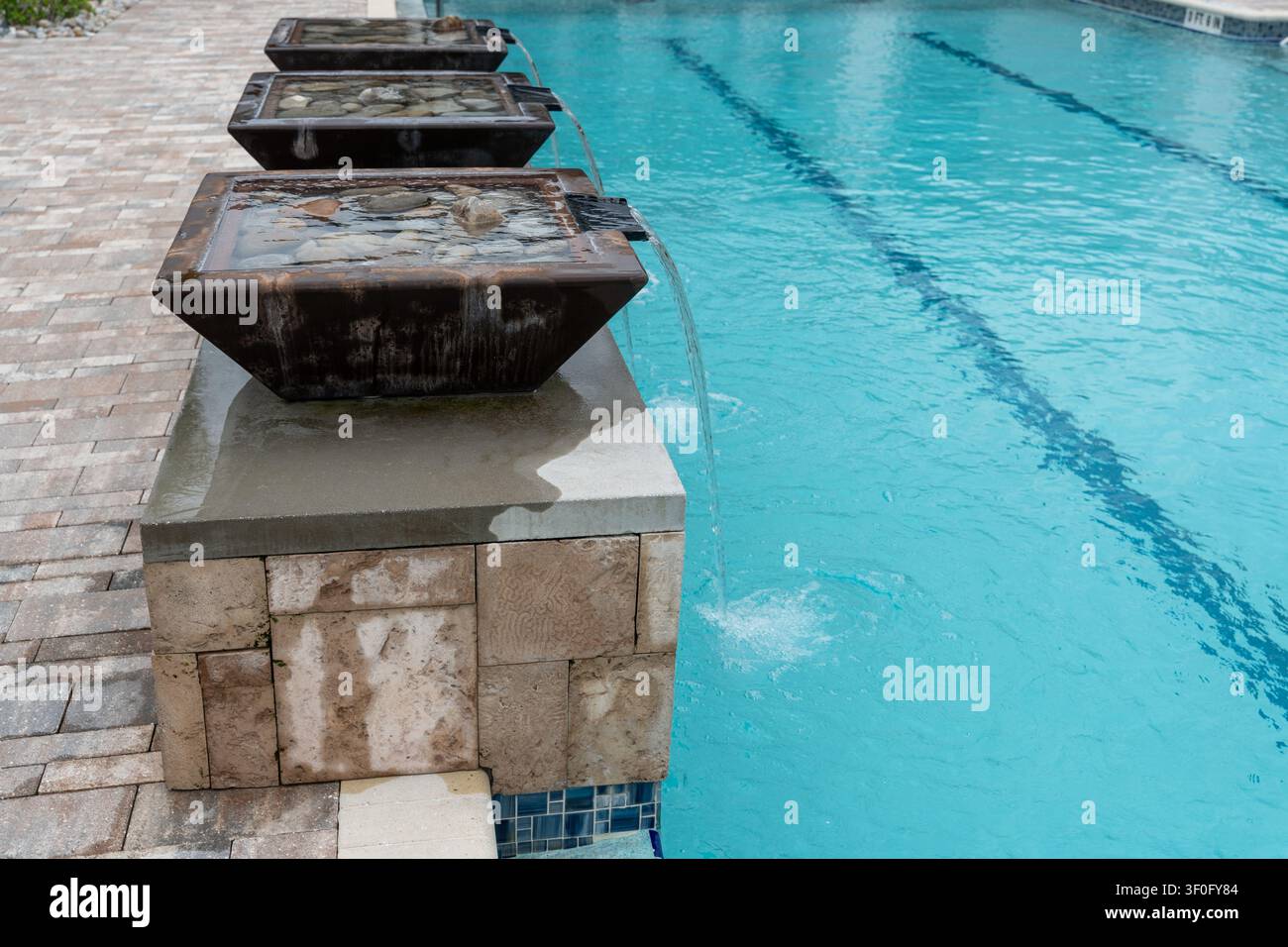 Foto orizzontale di quattro fontane in pietra che si riversano in una piscina blu cristallina, che mostra un design esterno di lusso e servizi in stile resort Foto Stock