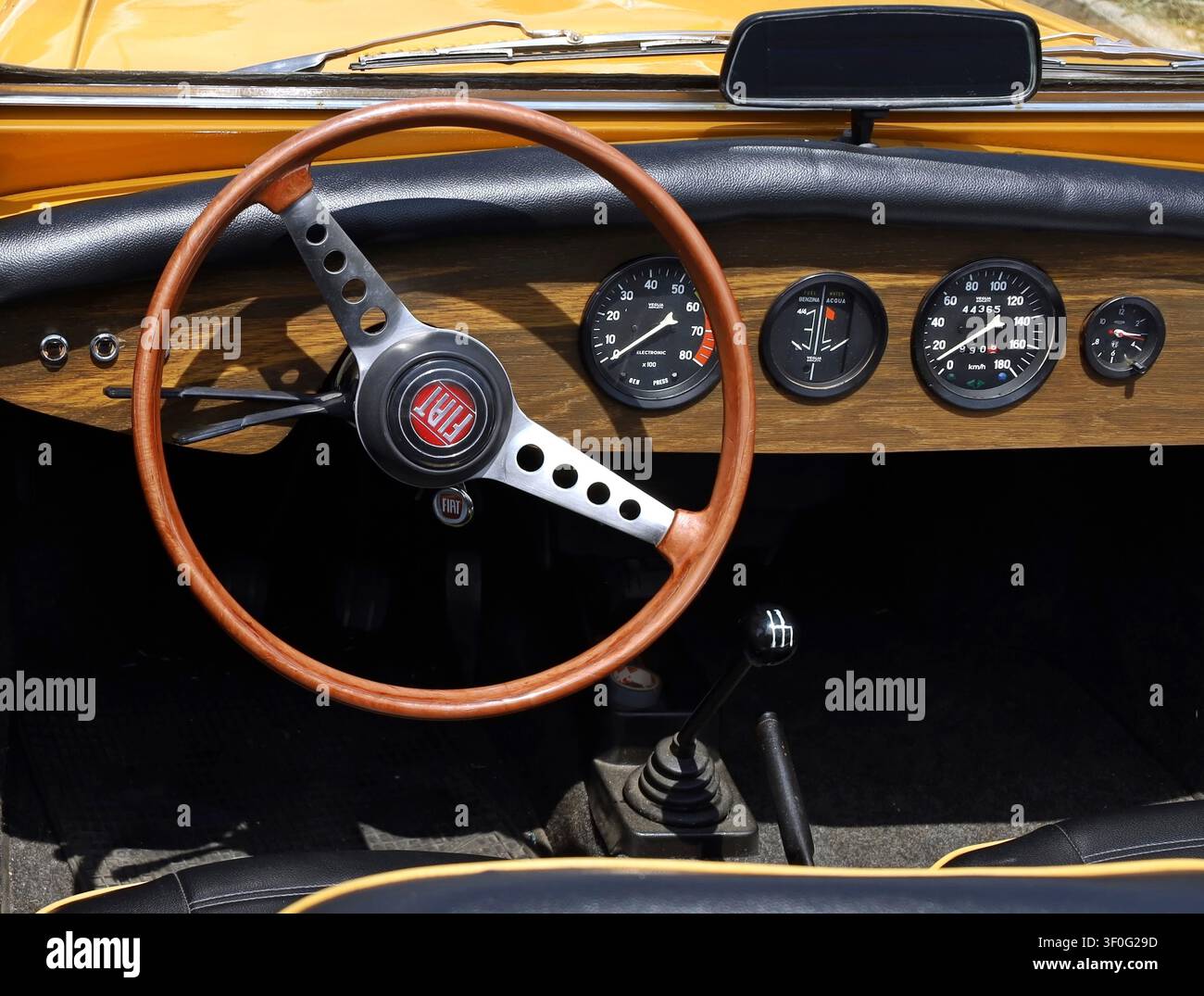 Azzida, Italia. Luglio, 6 2024. Logo Fiat sul volante in legno e sul cruscotto in legno di una spider vintage degli anni Sessanta durante un rally di auto classiche. Foto Stock