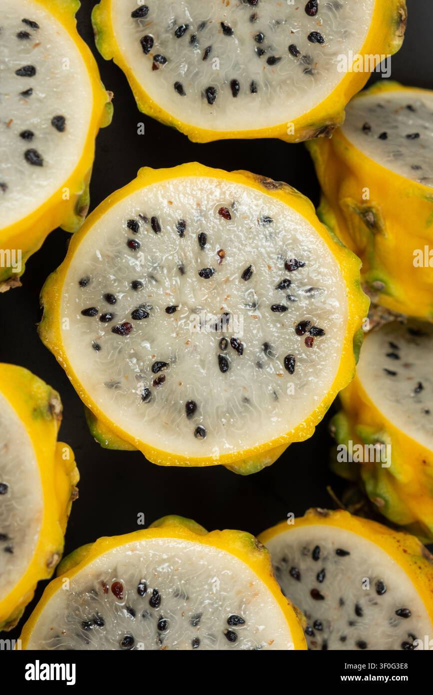 Frutta del drago gialla tagliata a metà che mostra la polpa bianca e i semi neri Foto Stock