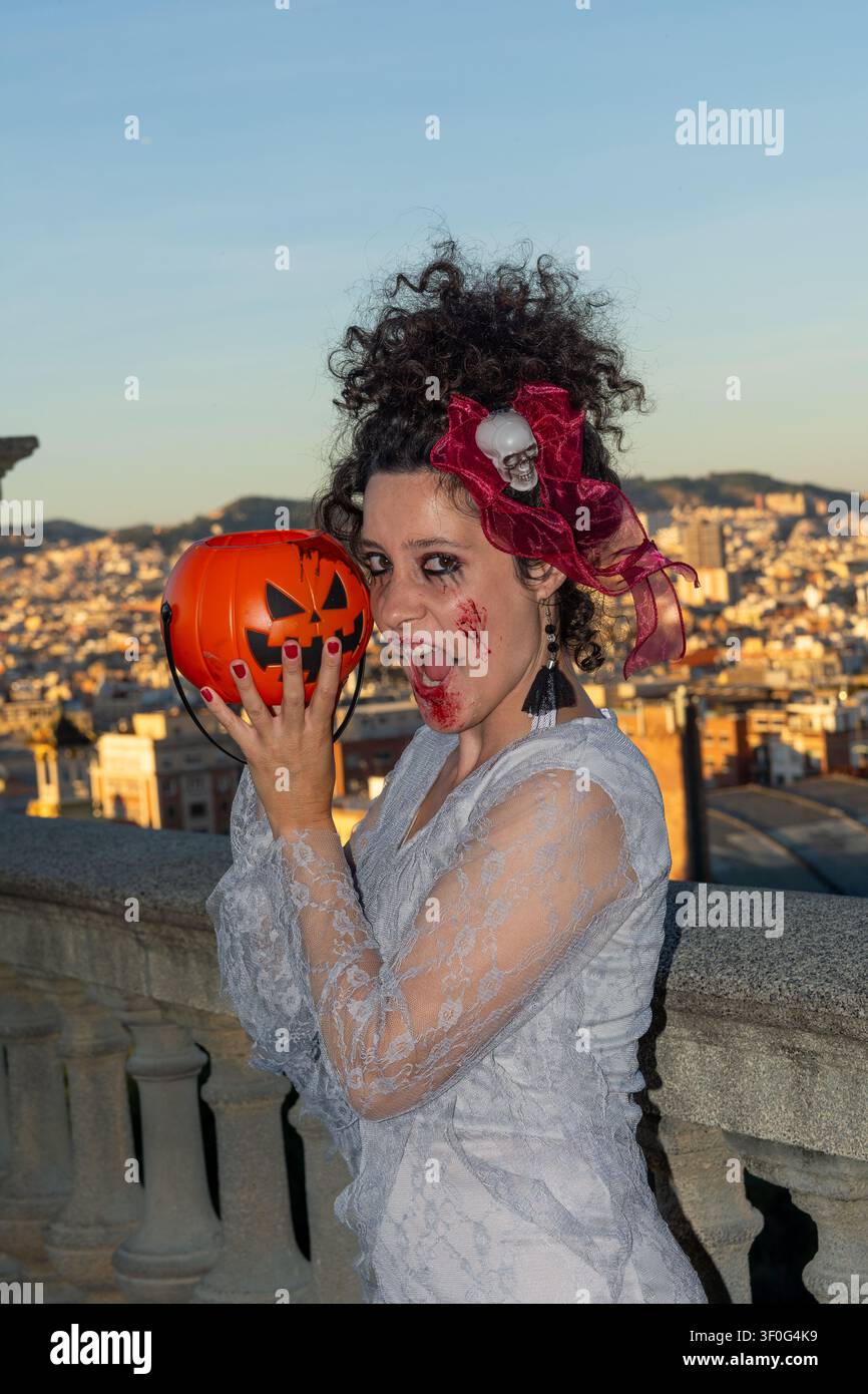Donna che posa in costume da zombie di Halloween tenendo un secchio di zucca Foto Stock