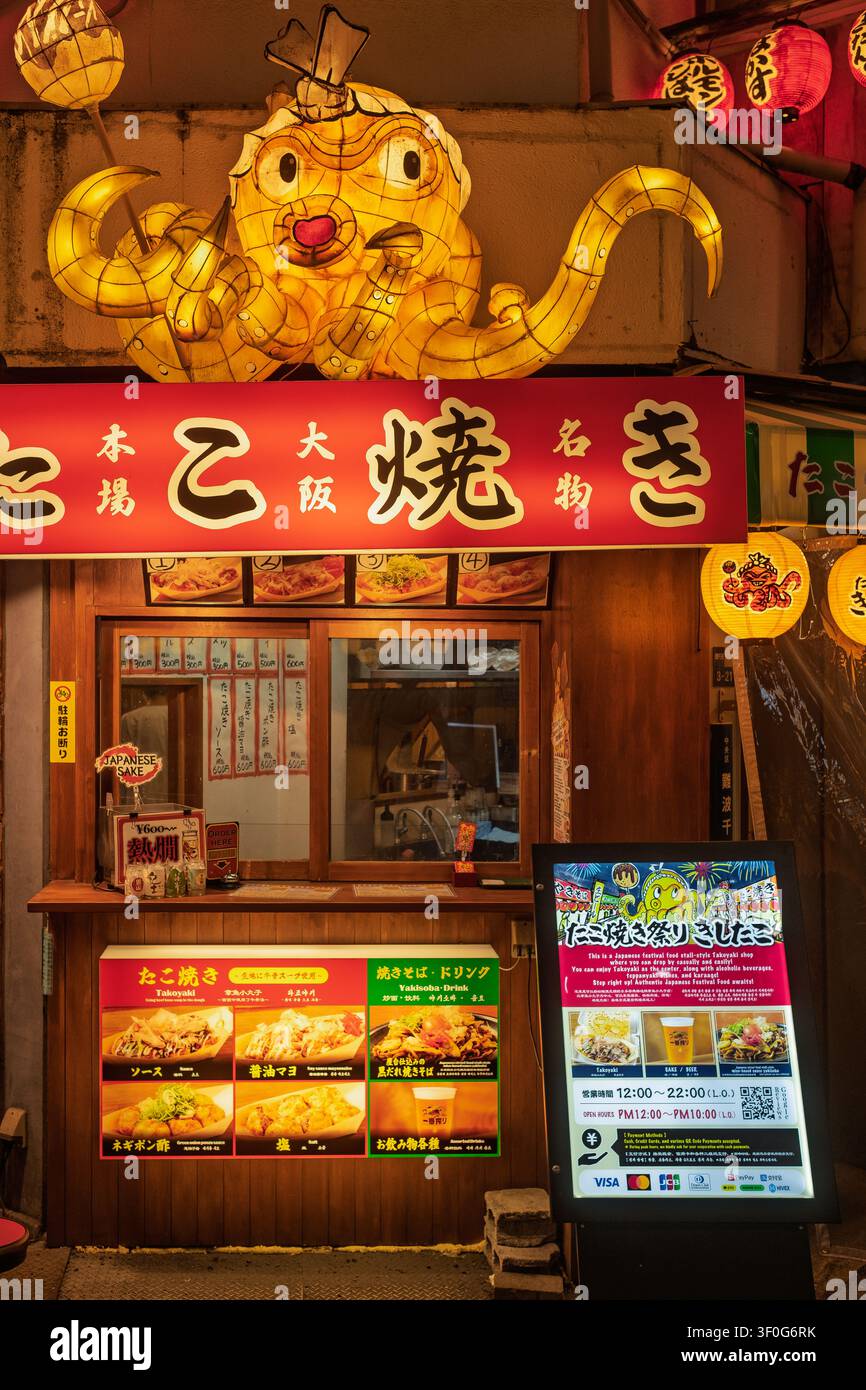 Un piccolo chiosco di street food con un cartello luminoso a forma di polpo giallo e una lavagna dei menu di notte, Osaka, Giappone Foto Stock