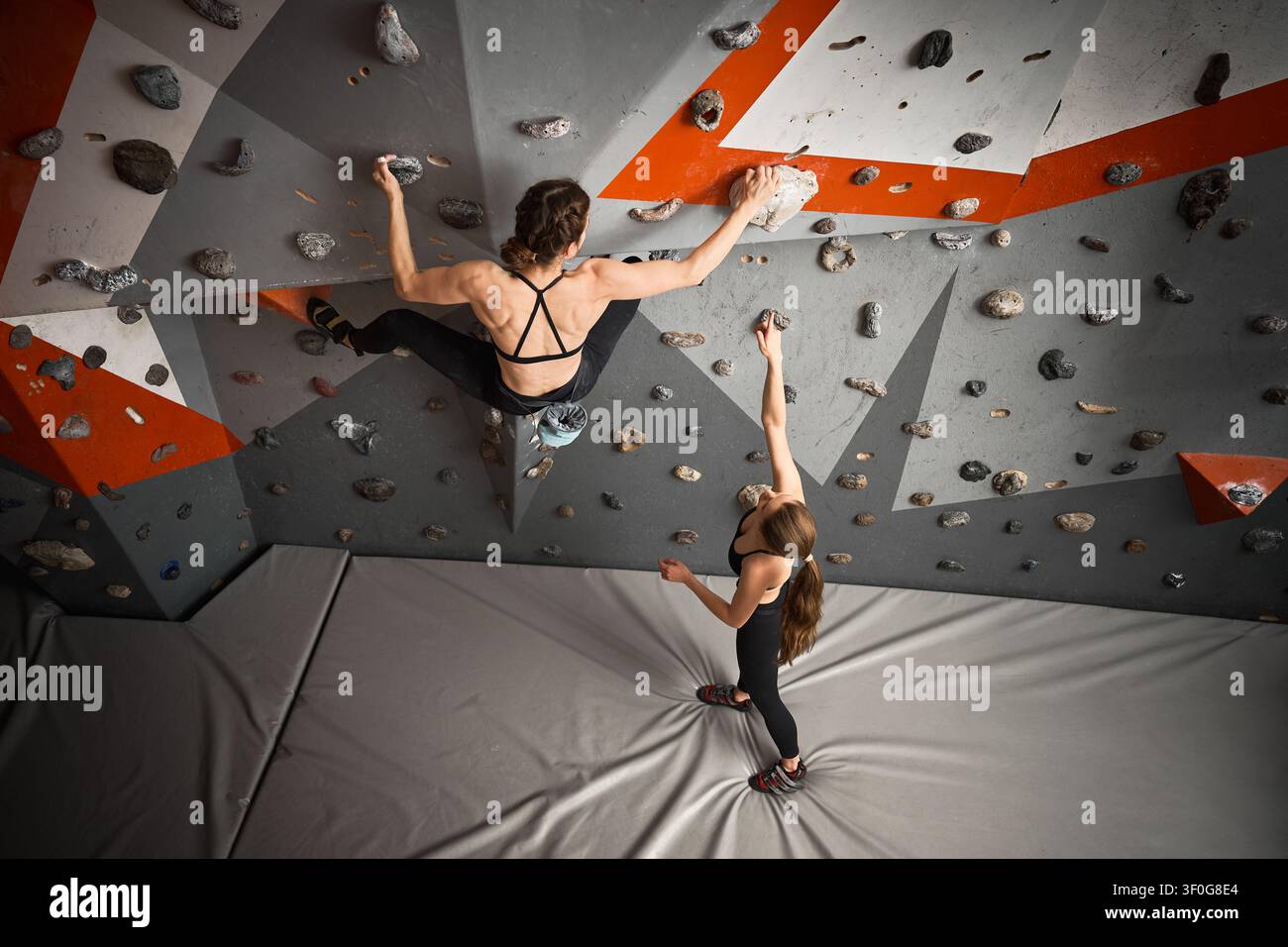 Due arrampicatrici lavorano su una via in una sala di bouldering indoor. Immagine per partnership, tecnica, fiducia, sfida, branding fitness, promozione del tempo libero Foto Stock