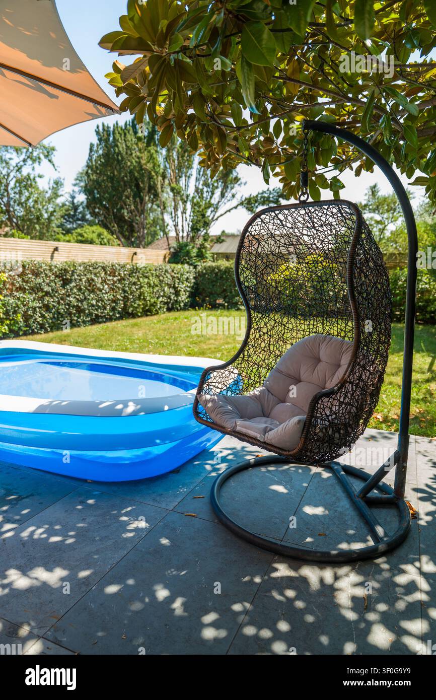 Sedia a uovo sospesa moderna vicino a una piscina gonfiabile nel cortile Foto Stock