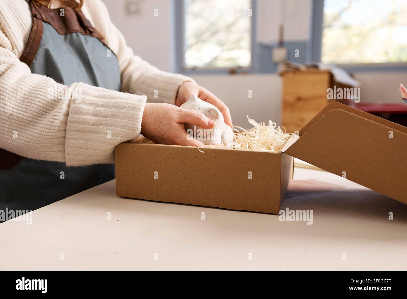 Proprietario di uno studio di ceramica che imballa una tazza in ceramica fatta a mano in una scatola regalo ecologica in uno spazio di lavoro di piccola impresa Foto Stock
