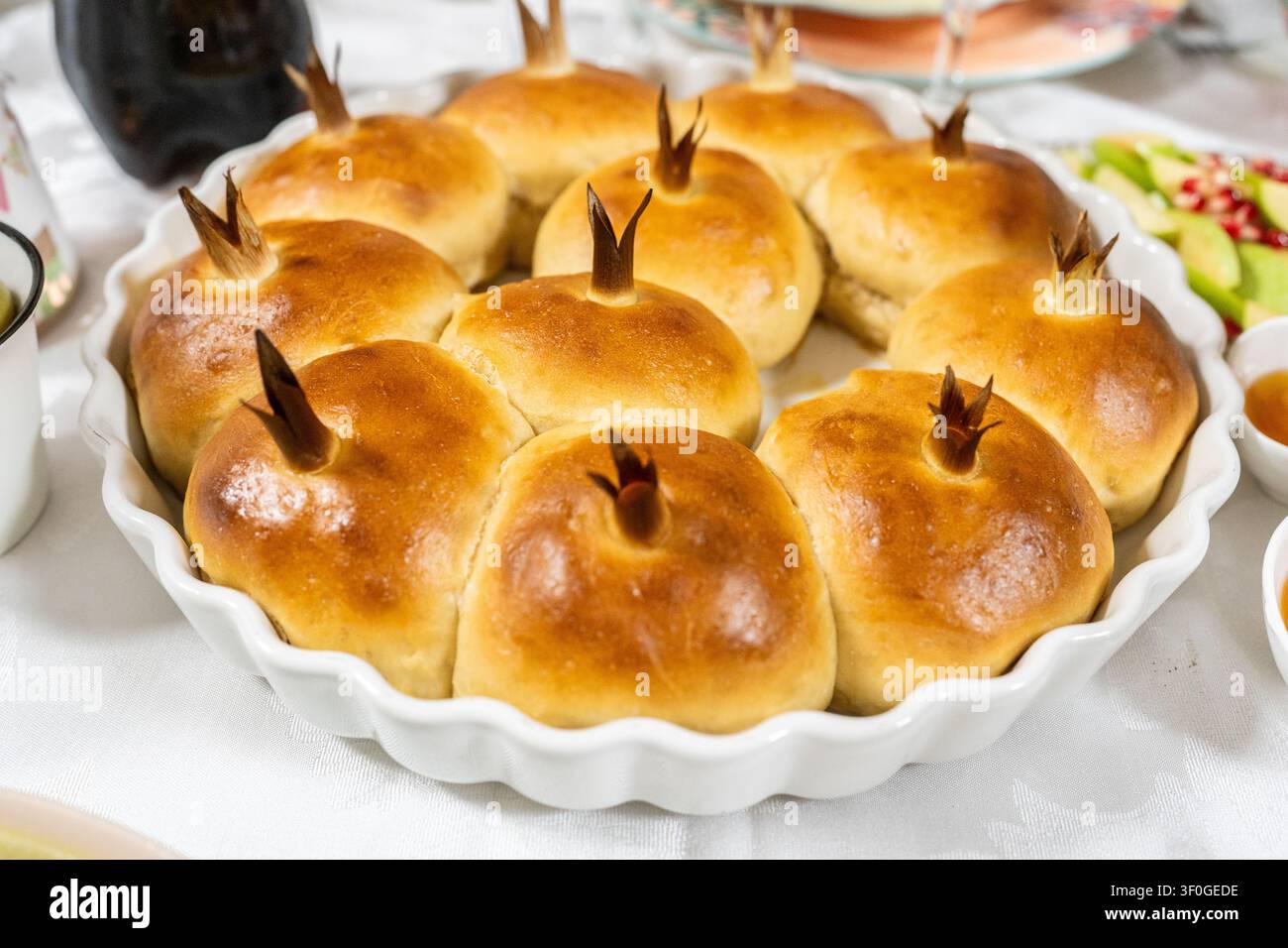 Panini di challah a forma di melograno dorato riposano su un piatto decorato, pronti per una dolce celebrazione ebraica del nuovo anno a Rosh Hashanah a casa. Foto Stock