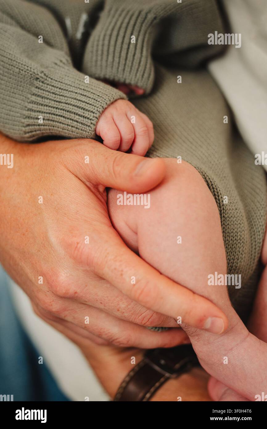 Primo piano di una mano adulta che tiene una gamba e una mano di un neonato Foto Stock