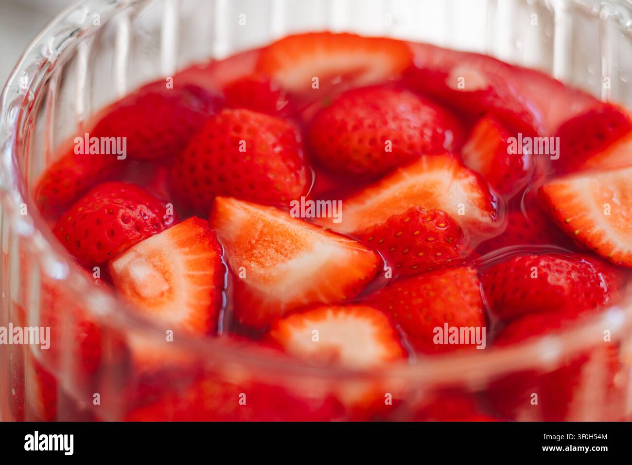 Fragole fresche affettate che si immergono nel succo in una ciotola di vetro Foto Stock