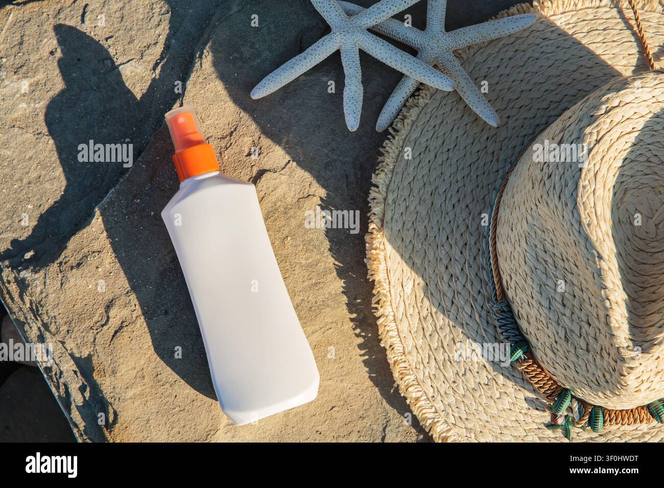 Mockup di spray solare vuoto con cappello da spiaggia su pietra illuminata dal sole Foto Stock