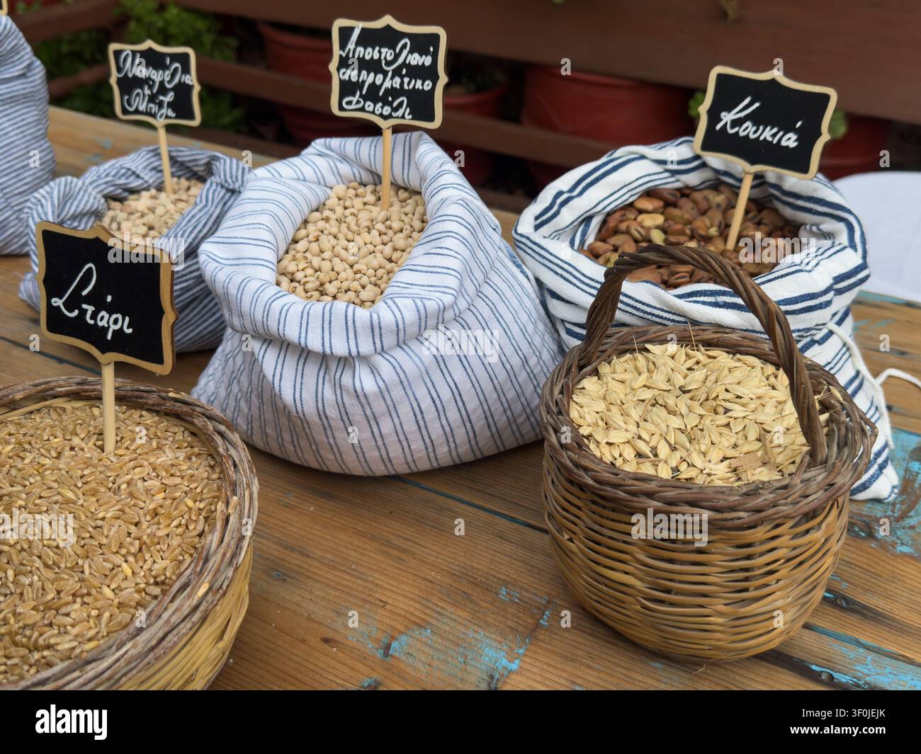 Legumi e cereali greci tradizionali in sacchi di stoffa e cesti di vimini con etichette per grano, piselli manarolia, fagioli bianchi di apostoliano, fave ecc. Foto Stock