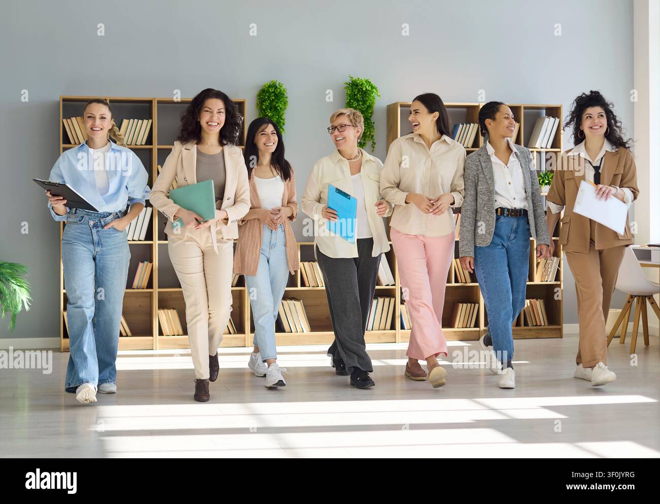 Squadra diversificata di donne d'affari sicure di sé che camminano insieme in un ufficio luminoso sorridendo Foto Stock
