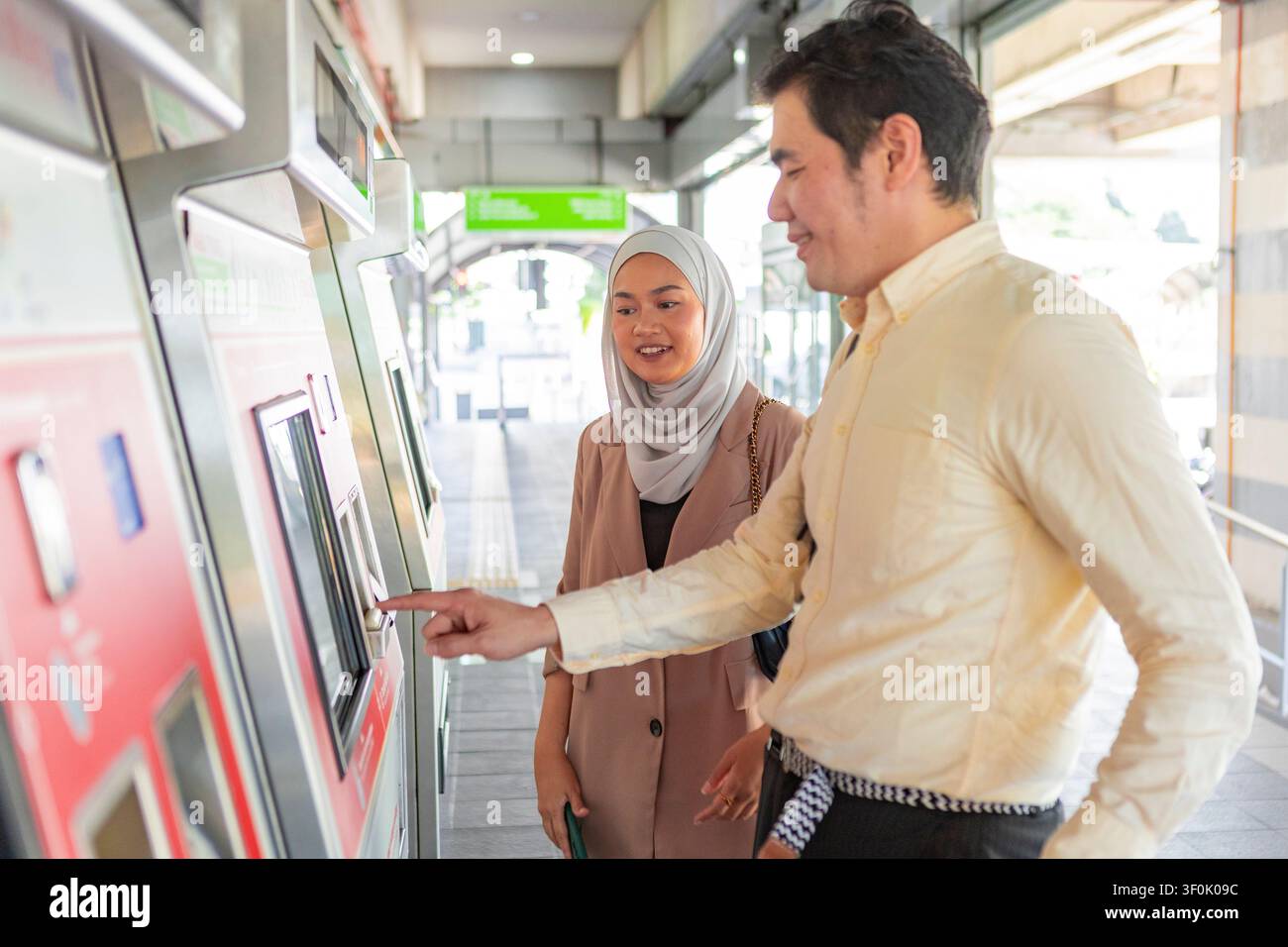 Due pendolari su un binario della stazione ferroviaria utilizzano un distributore automatico di biglietti self service, toccando lo schermo tattile per acquistare i biglietti, mostrando i mezzi di trasporto pubblici moderni Foto Stock