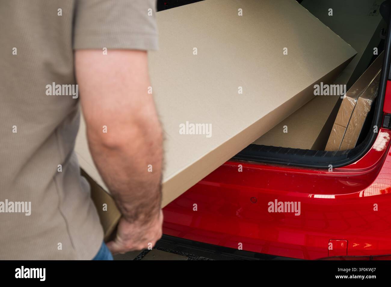 Trasporto di grandi fogli di cartone dal bagagliaio di un veicolo rosso per un progetto fai-da-te. Materiali ordinatamente organizzati visibili nell'auto, che migliorano un flusso di lavoro efficiente. Foto Stock