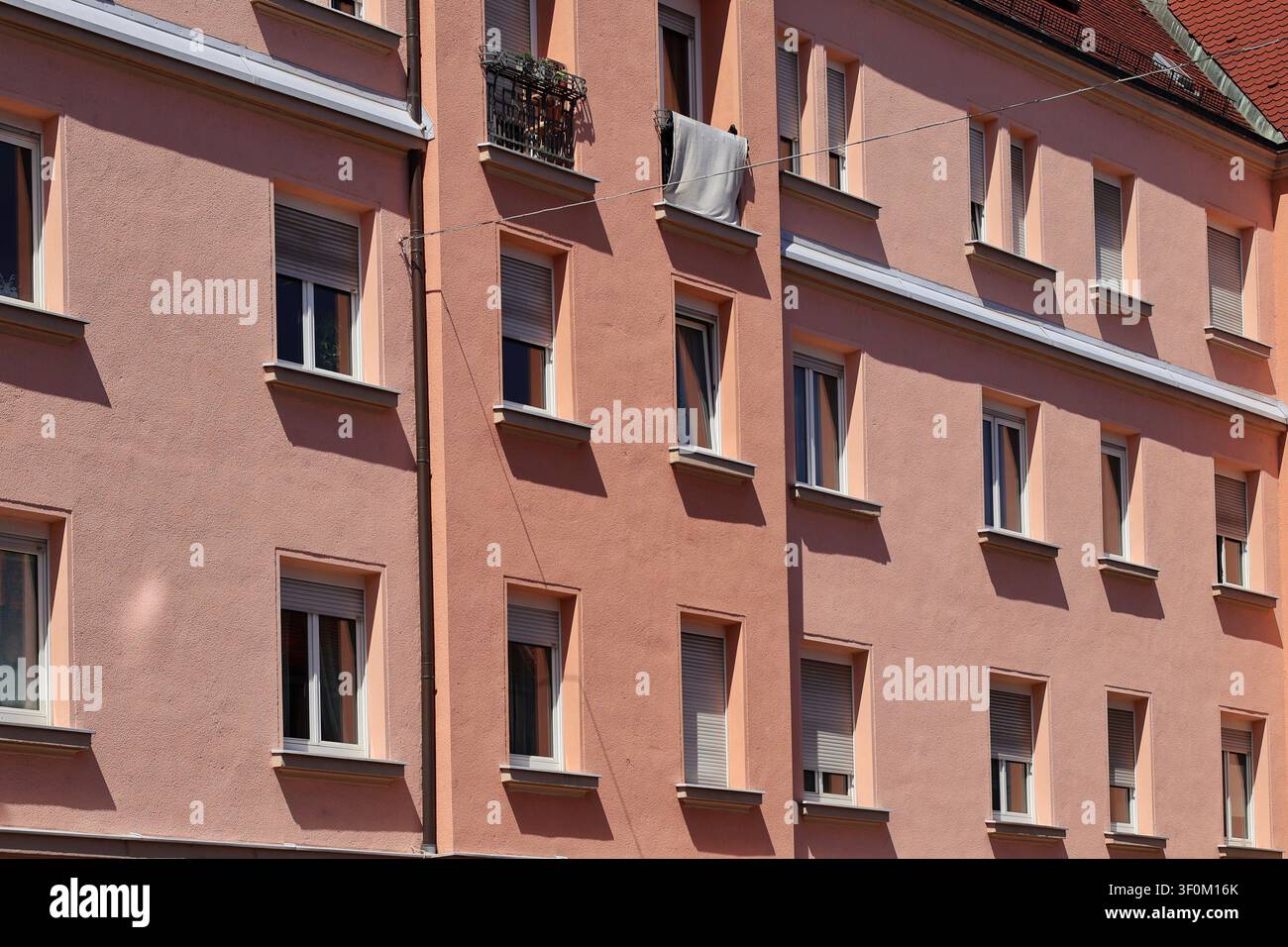 Facciata rosa di un edificio residenziale con finestre e ombre di luce solare intensa Foto Stock