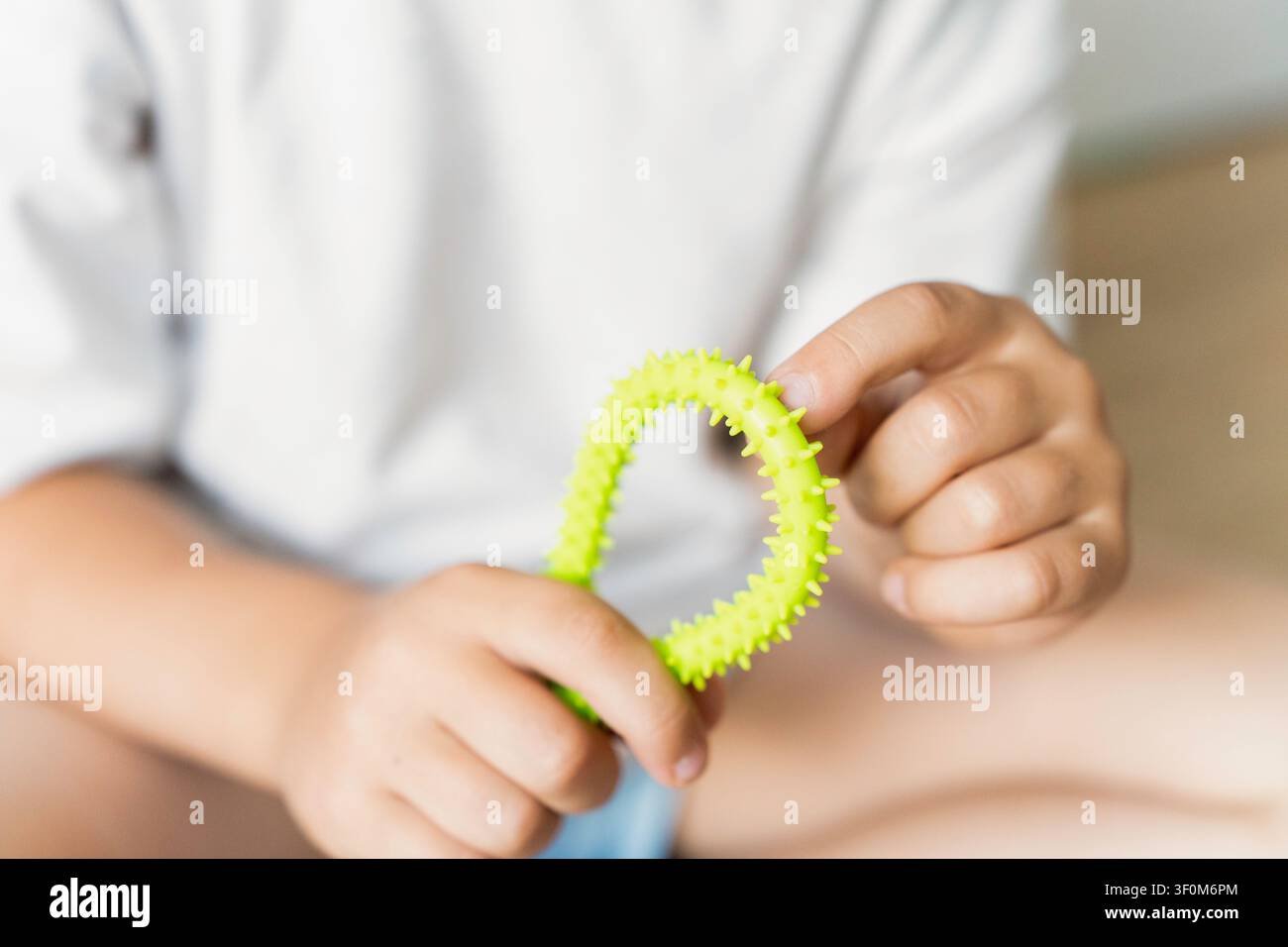 Primo piano di mani di bambino che toccano un giocattolo sensoriale verde strutturato, concetto di esplorazione tattile e abilità motorie. Foto Stock