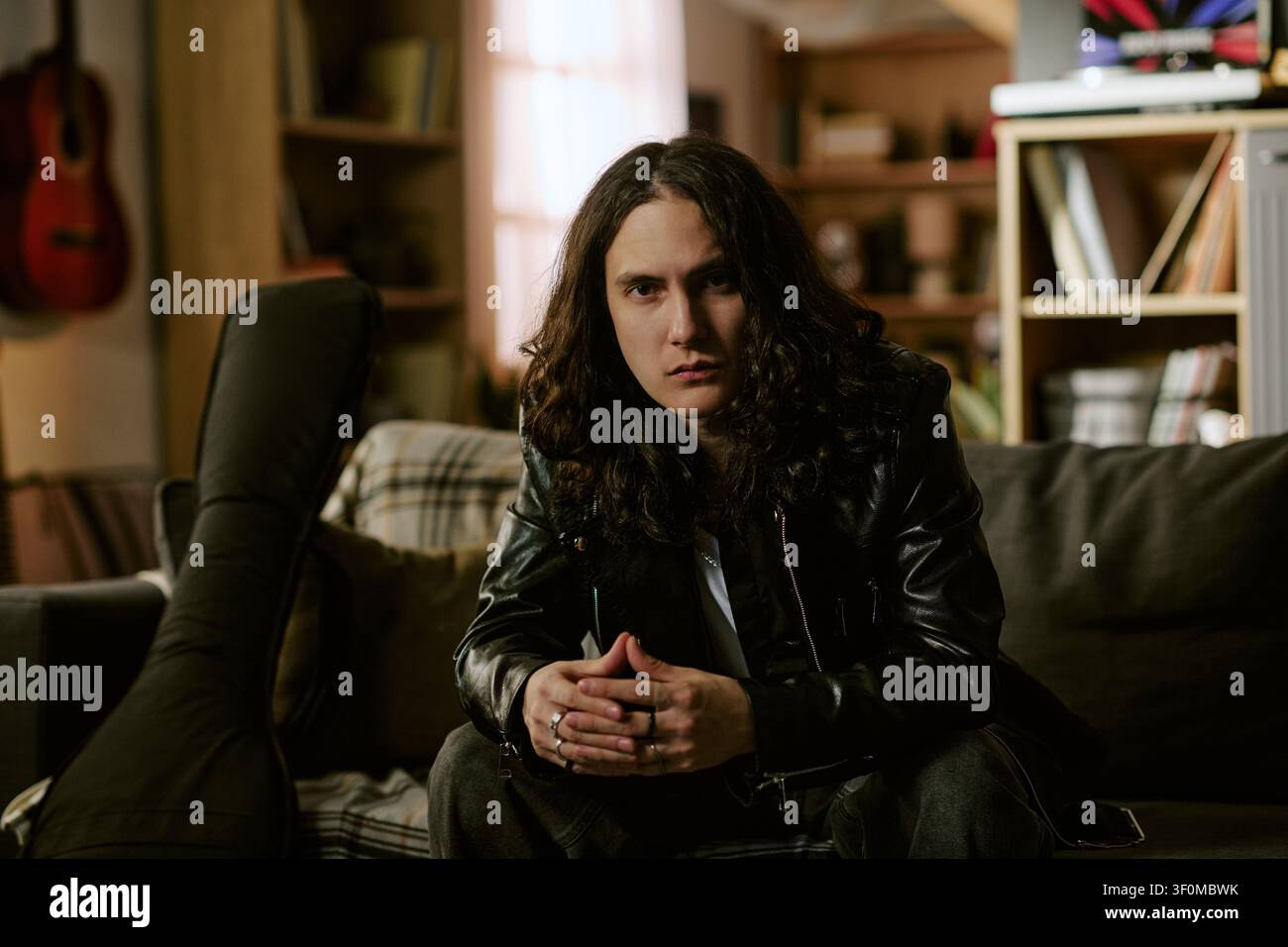 Ritratto di musicista maschio dai capelli lunghi seduto a casa per il branding artistico Foto Stock