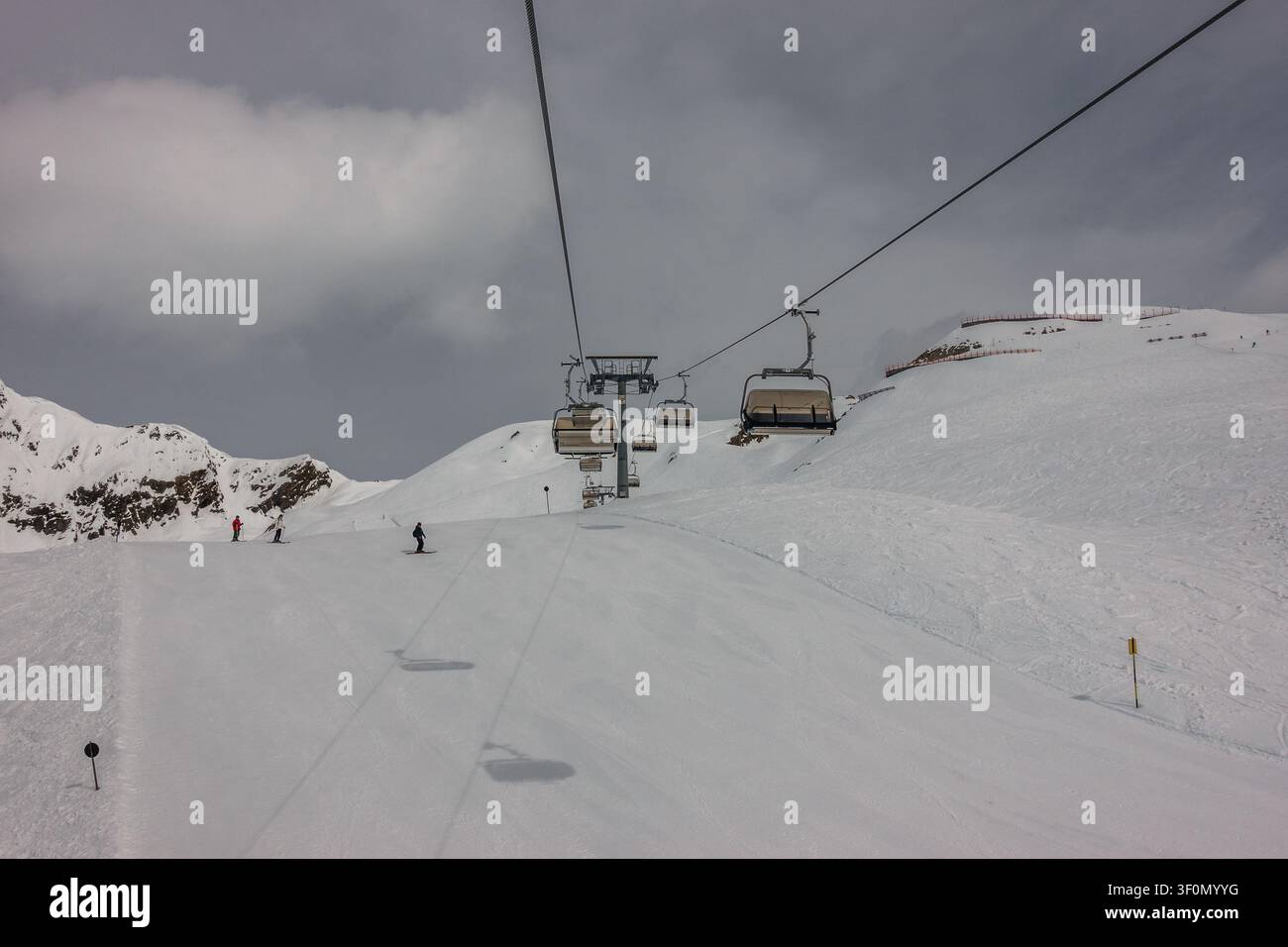 Gli sciatori scendono una vasta pista preparata sotto una seggiovia in funzione in una stazione sciistica alpina ad alta quota. Foto Stock