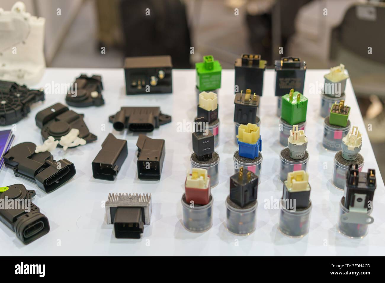 Prima di vari relè elettrici automobilistici, moduli di controllo e componenti elettronici disposti su un tavolo da esposizione bianco. Foto Stock