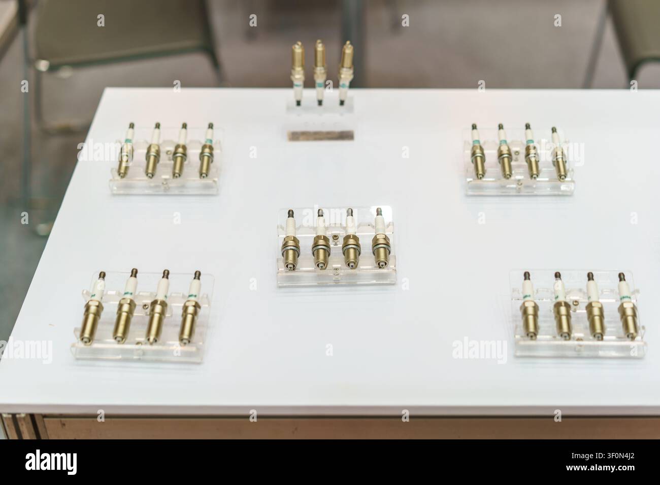 Una esposizione di nuove candele di accensione per motori automobilistici disposte su supporti in acrilico trasparente su un tavolo bianco, che mostra pezzi di ricambio per la manutenzione del veicolo Foto Stock