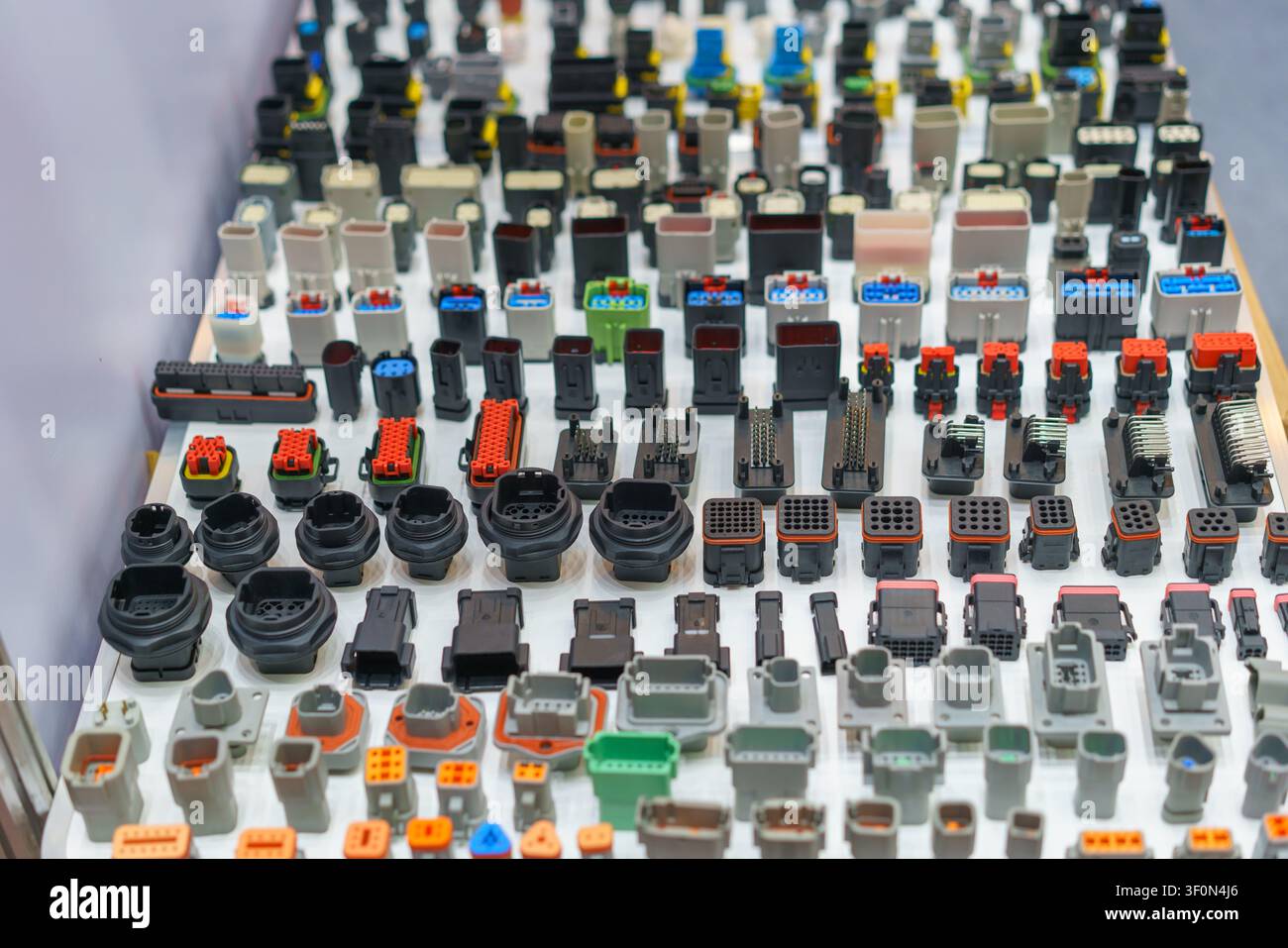Una grande esposizione di vari connettori, spine e prese di cablaggi elettrici industriali e automobilistici colorati disposti su un tavolo bianco. Foto Stock