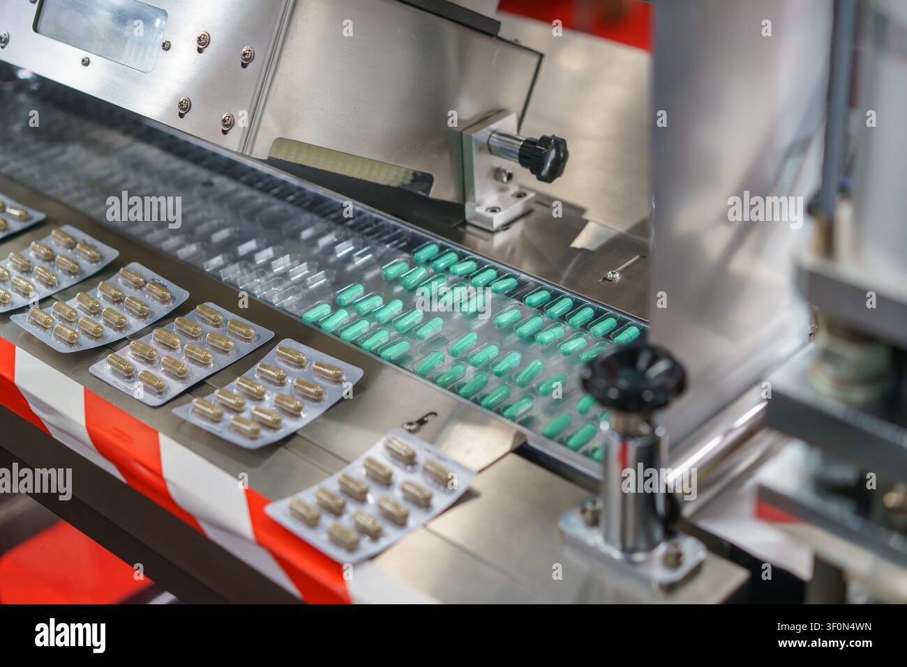 Prima vista di una macchina automatica per il confezionamento in blister industriale che elabora capsule di medicinali verdi e marroni su una linea di produzione in un'azienda farmaceutica Foto Stock