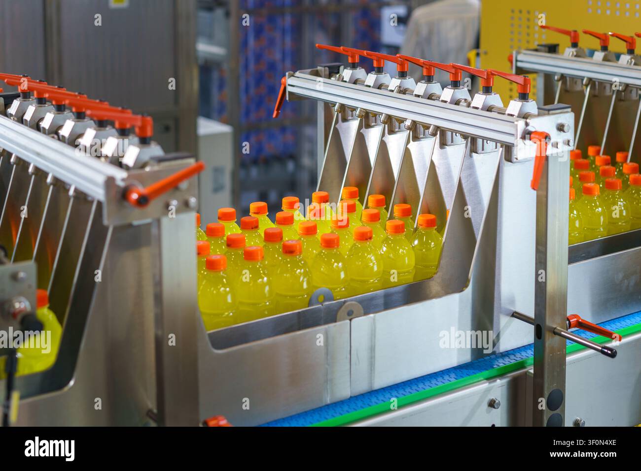 Macchina industriale automatica che smista bottiglie di plastica riempite con liquido giallo e tappi arancioni su un nastro trasportatore in una moderna fabbrica di bevande Foto Stock