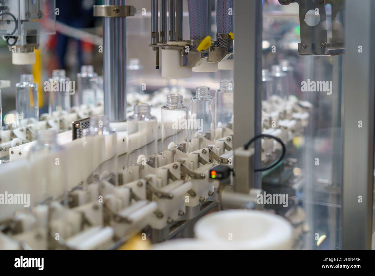 Primo piano di una macchina industriale automatizzata che elabora bottiglie di plastica trasparente su una linea di produzione moderna. L'attrezzatura utilizza ugelli precisi Foto Stock