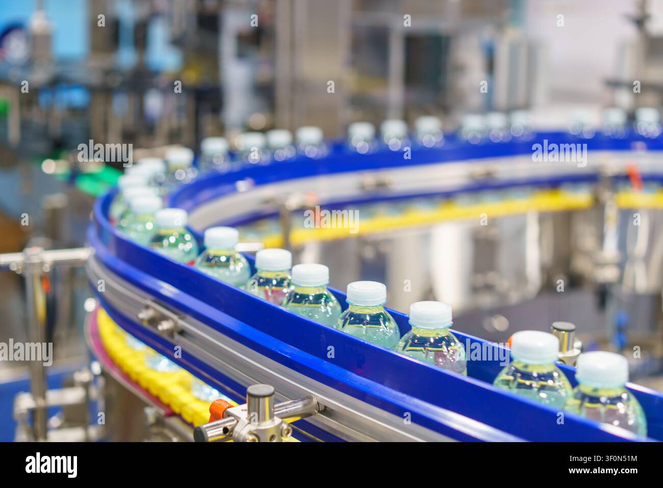 Centinaia di bottiglie di plastica trasparente piene di acqua potabile fresca che si muovono su un nastro trasportatore curvo su una linea di produzione automatizzata all'interno di un moderno Foto Stock