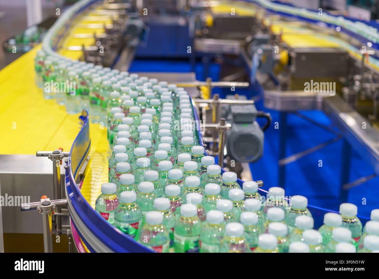 Centinaia di bottiglie di plastica trasparente piene di acqua potabile fresca che si muovono su un nastro trasportatore curvo su una linea di produzione automatizzata all'interno di un moderno Foto Stock