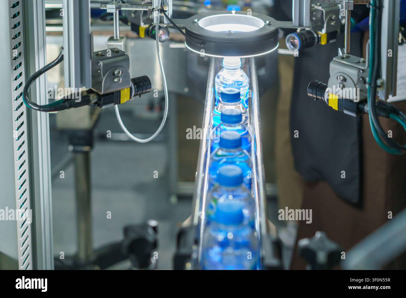 Prima piano di una macchina per l'etichettatura automatica che applica etichette di carta bianca su bottiglie di plastica che avanzano su un nastro trasportatore in un moderno stabilimento di produzione. Foto Stock