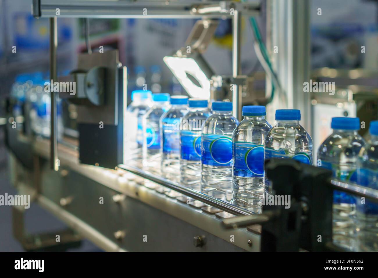 Primo piano di una linea di produzione automatizzata con bottiglie d'acqua di plastica. Un sistema di visione meccanica con una luce intensa ispeziona una bottiglia per il controllo qualità Foto Stock