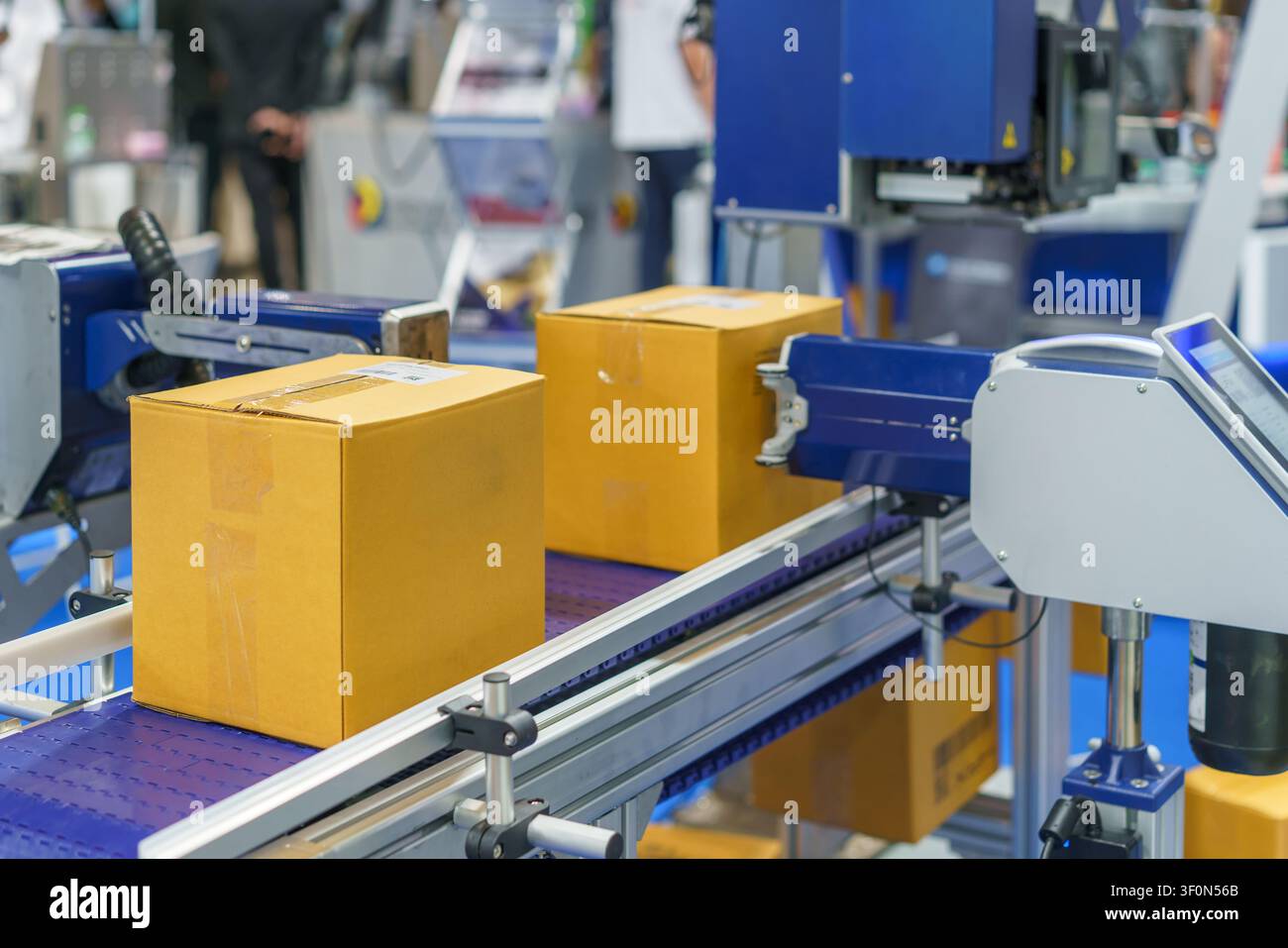 Scatole di cartone che si muovono su un nastro trasportatore oltre una macchina da stampa industriale automatizzata che applica codici a barre e testo in una moderna logistica o manifattura Foto Stock