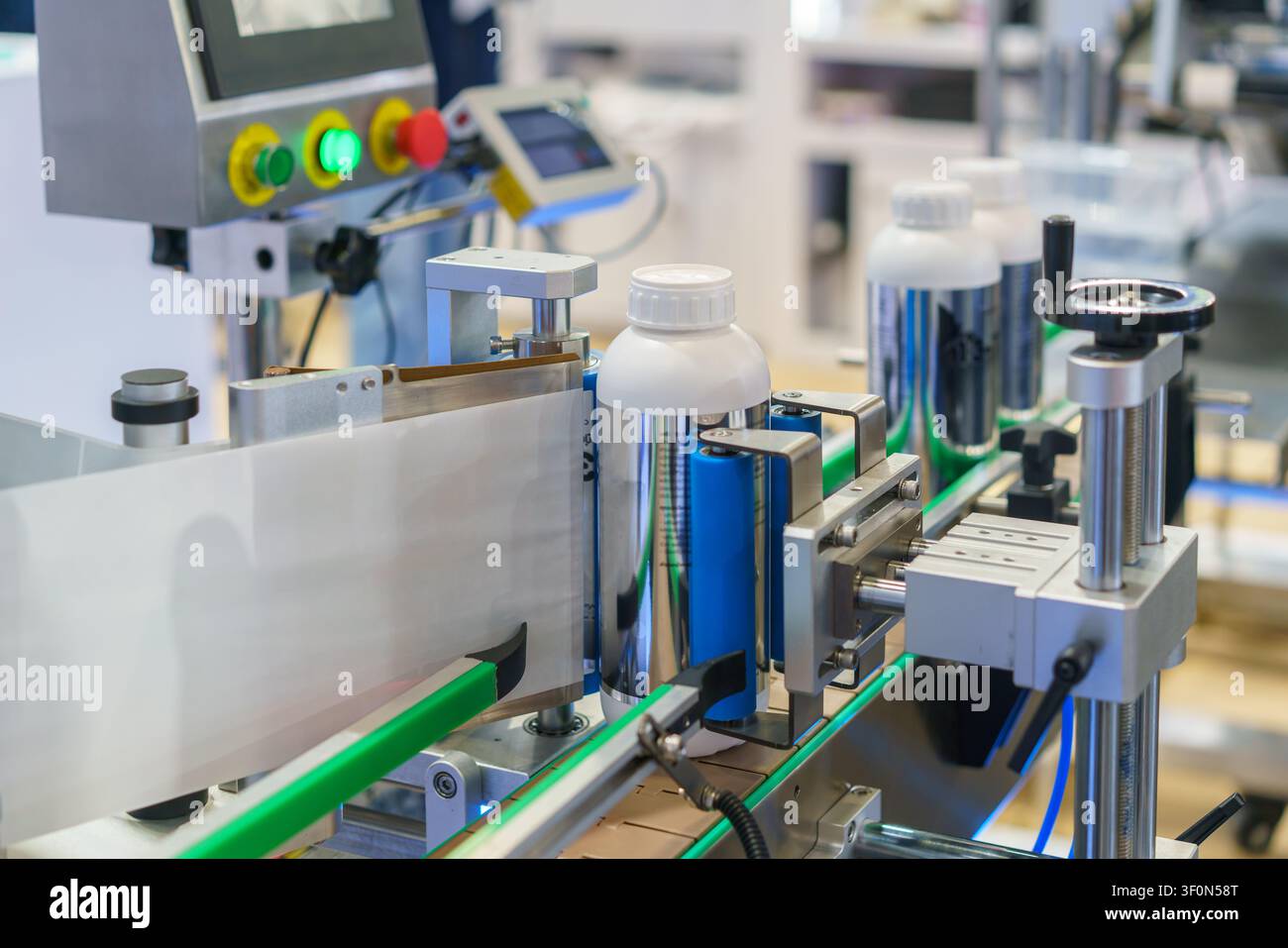Prima piano di una macchina per l'etichettatura automatica che applica etichette di carta bianca su bottiglie di plastica che avanzano su un nastro trasportatore in un moderno stabilimento di produzione. Foto Stock