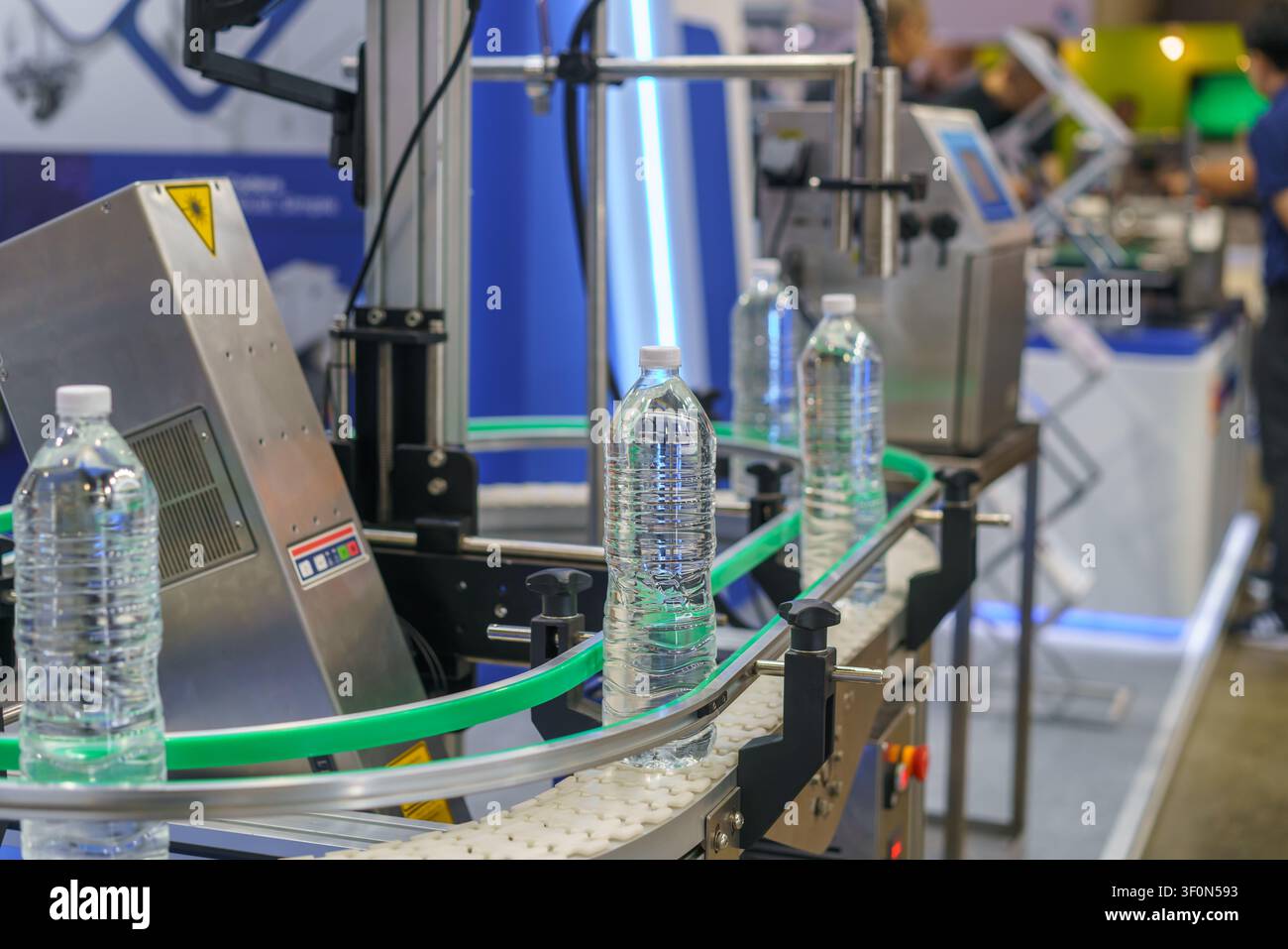 una linea di produzione automatizzata con bottiglie d'acqua di plastica. Un sistema di visione artificiale con una luce intensa ispeziona una bottiglia per il controllo qualità in una fabbrica Foto Stock