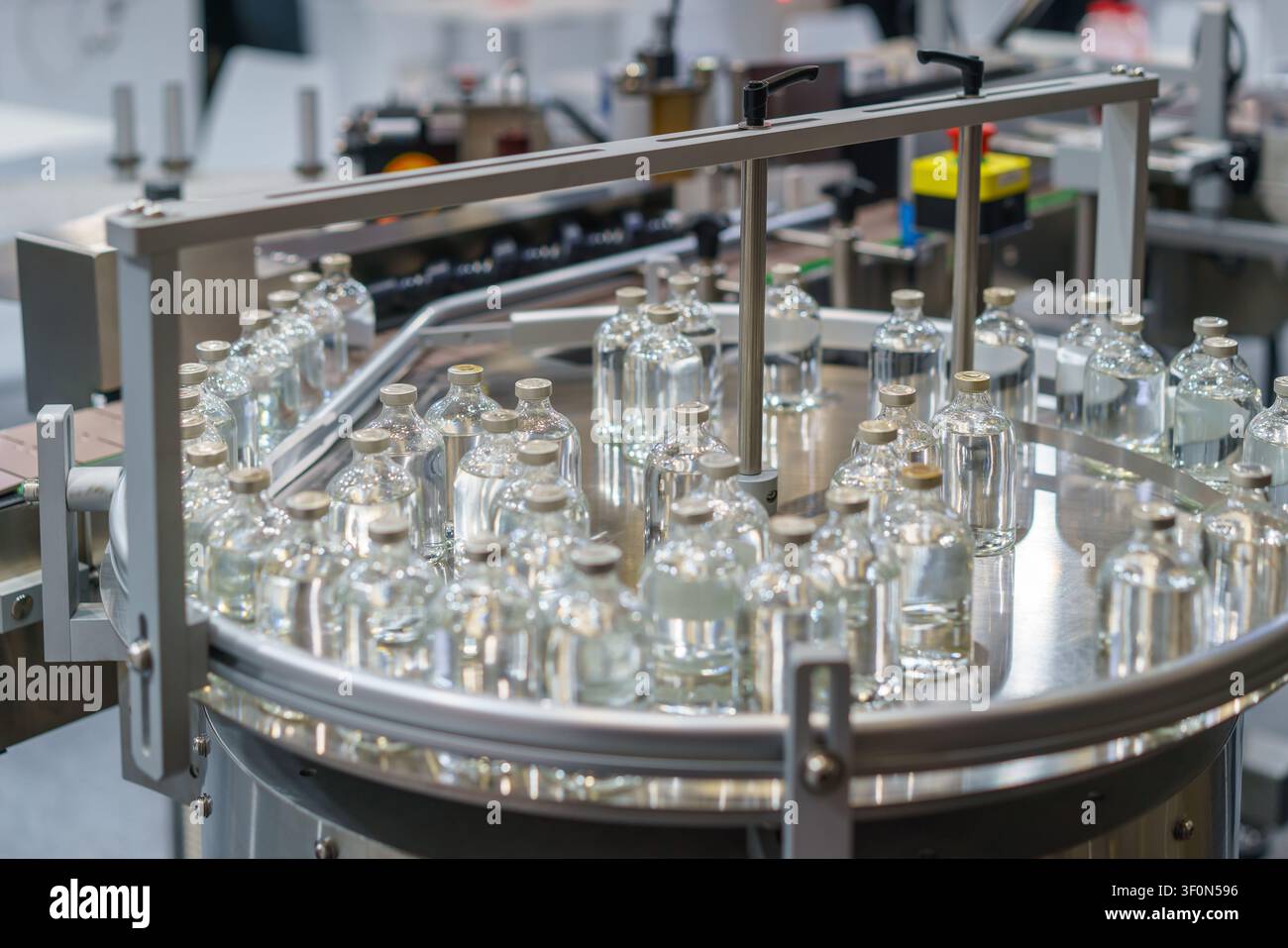 Fiale di vetro trasparente riempite con liquido che si muovono su un tavolo di accumulo rotativo in acciaio inossidabile in una linea di produzione farmaceutica automatizzata. Foto Stock