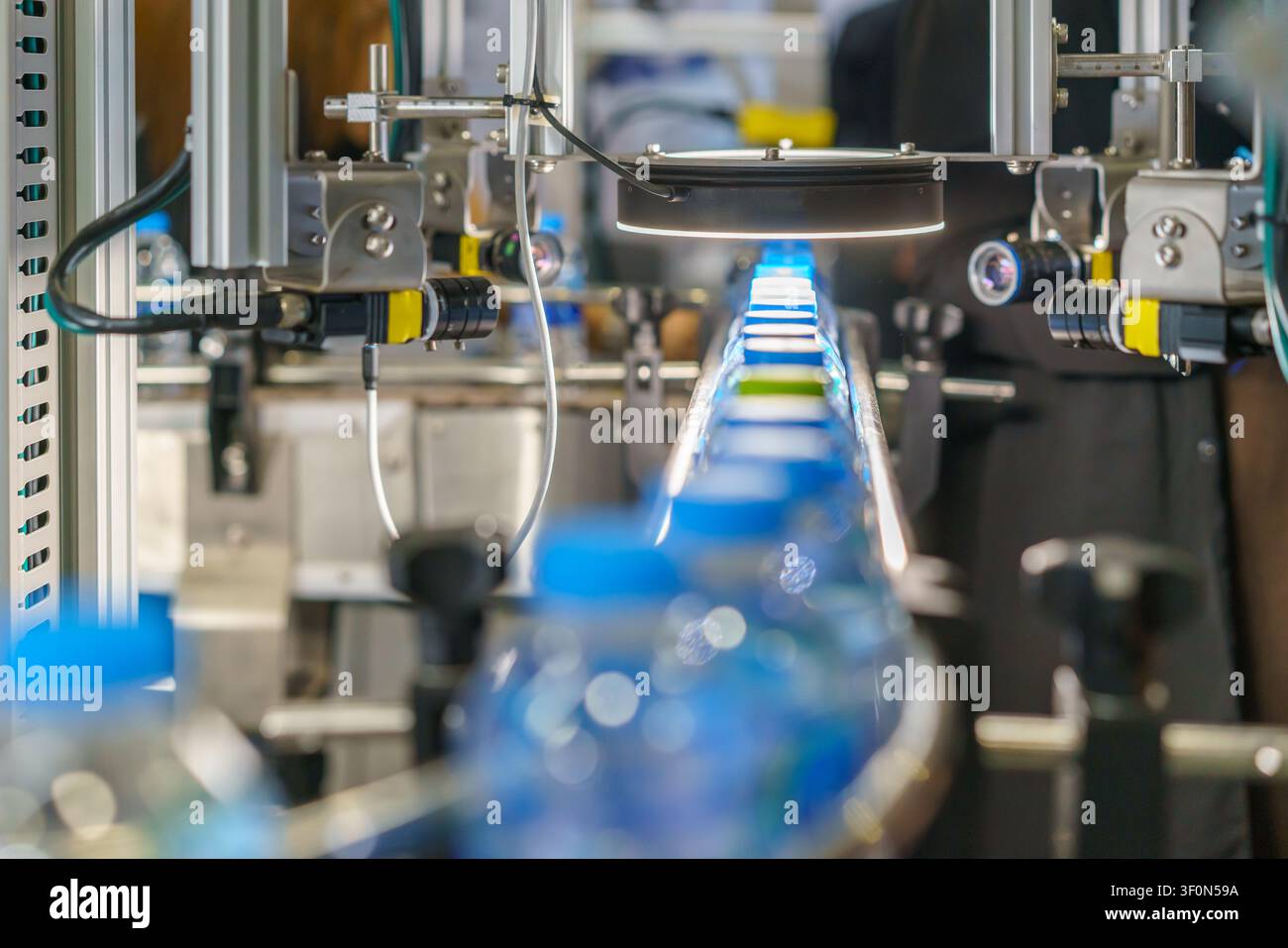 Primo piano di una linea di produzione automatizzata con bottiglie d'acqua di plastica. Un sistema di visione meccanica con una luce intensa ispeziona una bottiglia per il controllo qualità Foto Stock