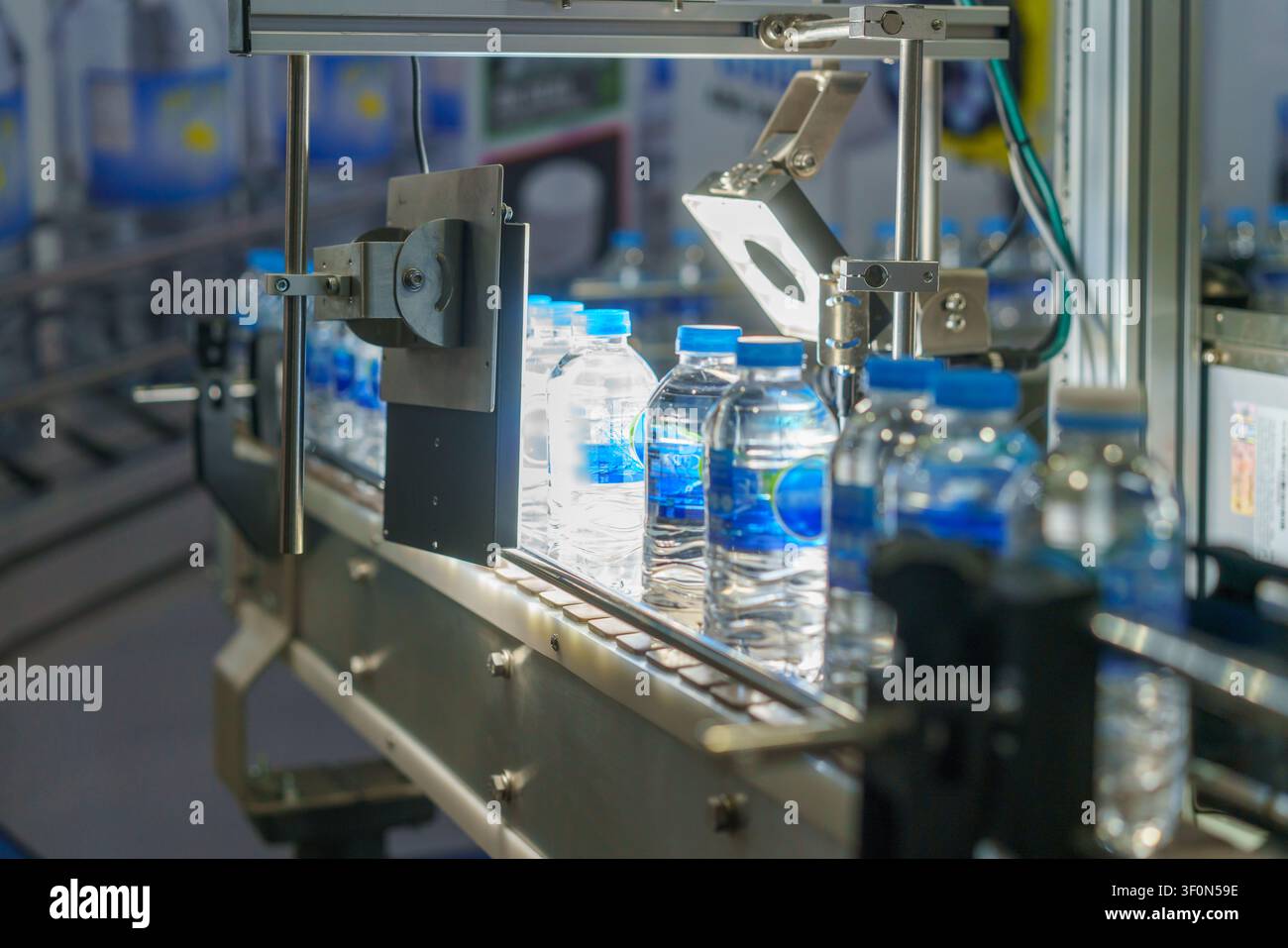 Primo piano di una linea di produzione automatizzata con bottiglie d'acqua di plastica. Un sistema di visione meccanica con una luce intensa ispeziona una bottiglia per il controllo qualità Foto Stock