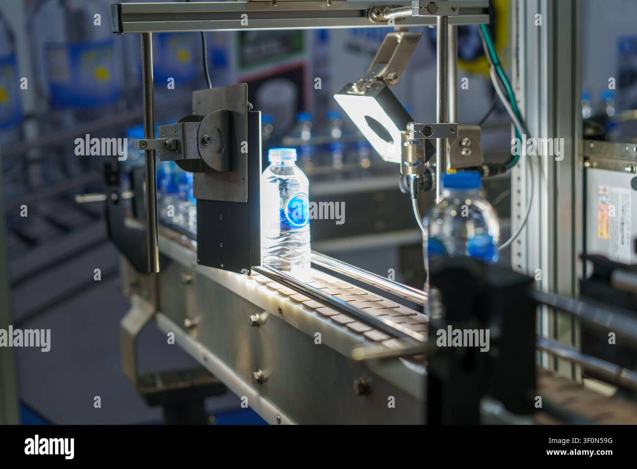 Primo piano di una linea di produzione automatizzata con bottiglie d'acqua di plastica. Un sistema di visione meccanica con una luce intensa ispeziona una bottiglia per il controllo qualità Foto Stock